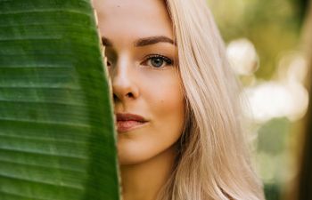 Beautiful blonde-haired woman hiding half of her face behinf a big palm leaf., 