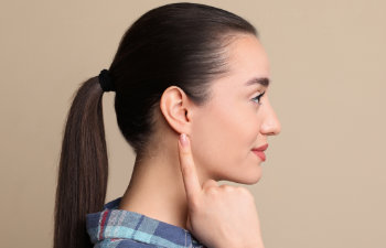 young woman pointing at her ear on beige background, 