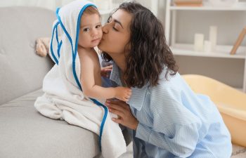 Happy mother kissing her baby in towel on sofa after bathing at home, 