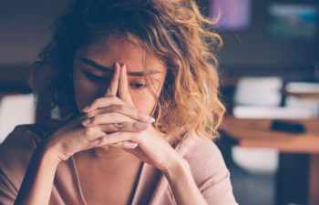 Closeup of sad young Asian woman at cafe leaning head on clasped hands and staring into vacancy., 